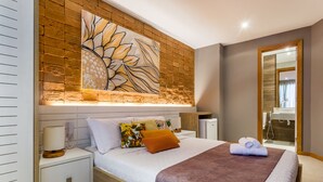 A modern bedroom with a large bed, a nightstand, a bedside table, a wall-mounted artwork, and a bathroom visible through an open door. - Bravo Pousada Design (Cabo Frio)