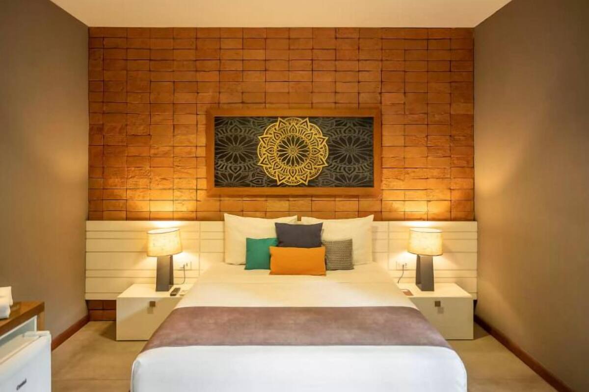 Une chambre d’hôtel avec une tête de lit ornée d’un motif en briques, un grand élément décoratif mural, un lit avec de nombreux oreillers et des lampes de chevet.