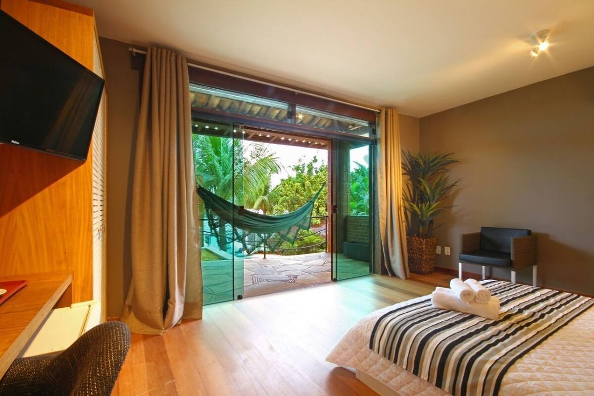 Une chambre avec un lit, une télévision, une chaise, un hamac et une vue sur la verdure.
