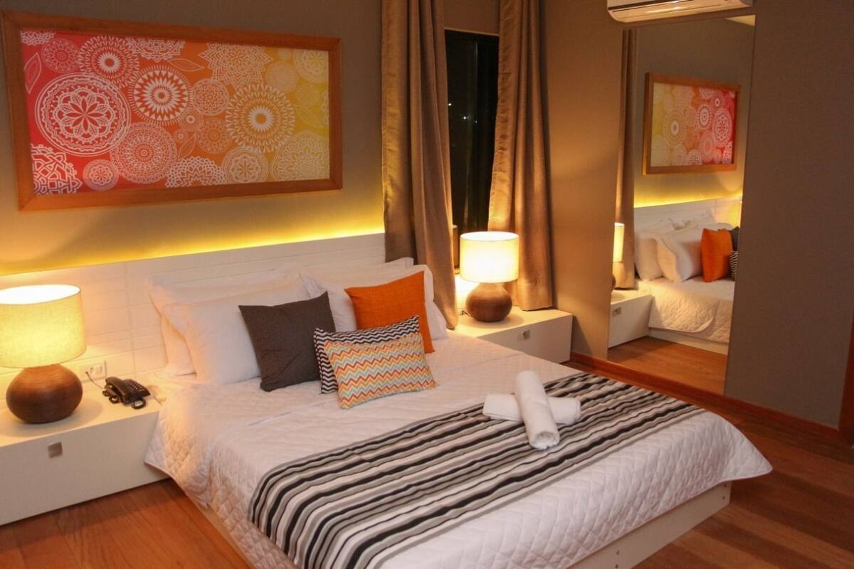 Une chambre d’hôtel équipée d’un lit, de lampes de chevet, d’un téléphone, d’un miroir et d’une œuvre d’art murale.