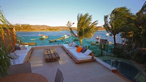 A poolside area with a wooden deck, lounge chairs, and a view of boats on the water. - Bravo Pousada Design (Cabo Frio)