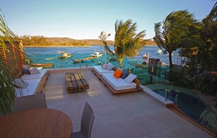 Zona de piscina con terraza de madera, sillas de descanso y vista a barcos en el agua.