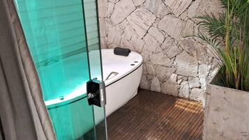 Un baño moderno con un jacuzzi de vidrio, pared de piedra y suelo de madera.