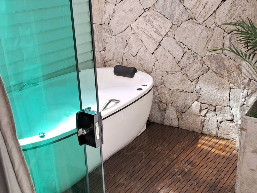 Un baño moderno con un jacuzzi de vidrio, pared de piedra y suelo de madera.