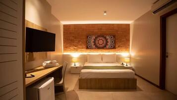A hotel room with a bed, bedside lamps, a flat-screen TV, a desk with a chair, and a small refrigerator.