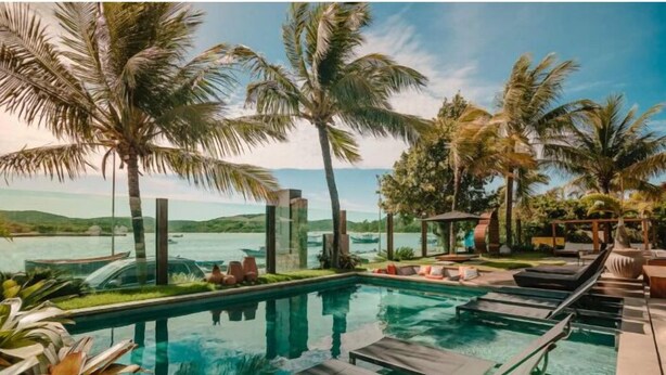 A poolside area with lounge chairs, palm trees, and a view of the water. - Bravo Pousada Design (Cabo Frio)