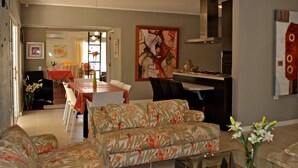 A living room with a sofa, a dining table with chairs, and a kitchen area with a stove. - Parrot Villa (Oranjestad)