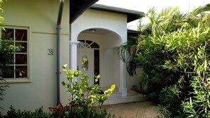 A house with a white exterior, a number '36' on the wall, and a front porch with steps leading to an arched doorway. - Parrot Villa (Oranjestad)