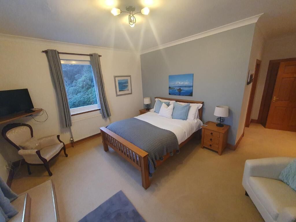 Une chambre à coucher avec un lit, des tables de chevet, une chaise, un téléviseur et une fenêtre avec des rideaux.