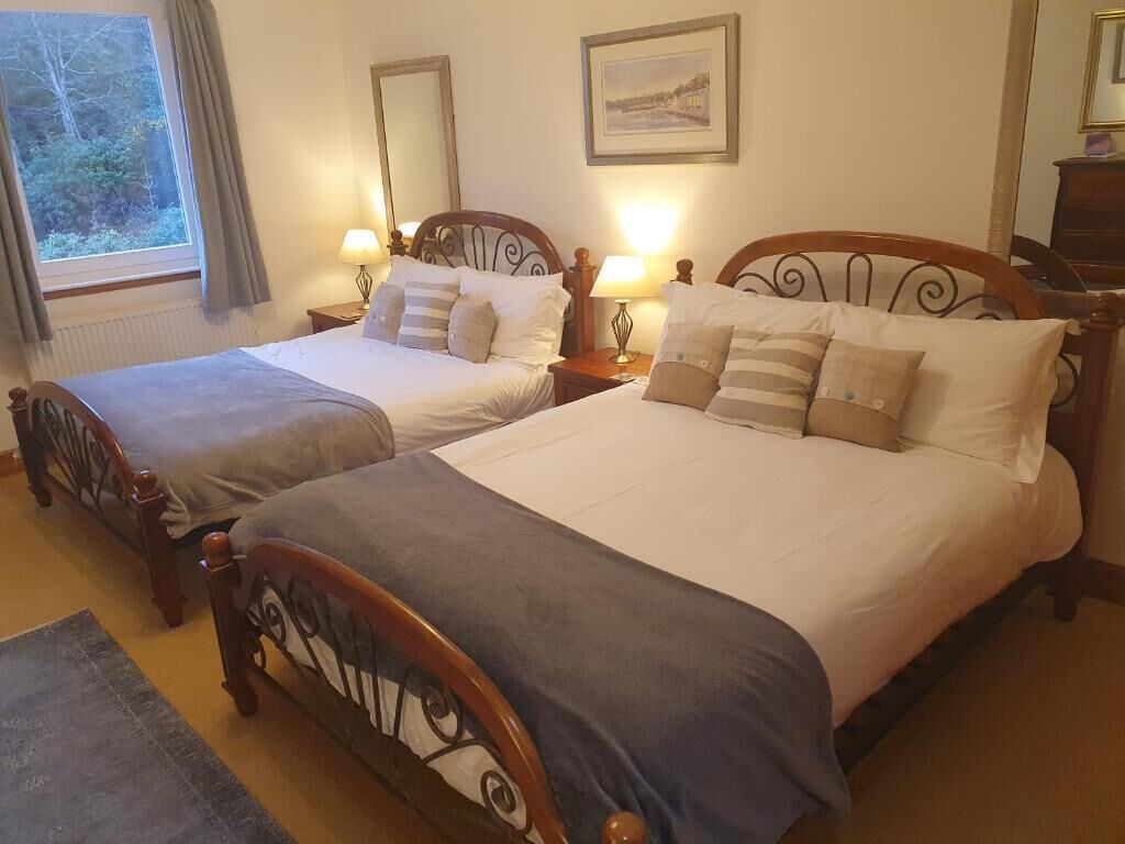 Una habitación de hotel con dos camas individuales, una ventana con cortinas, una mesita de noche con lámpara y un cuadro enmarcado en la pared.
