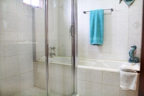 A bathroom with a glass-enclosed shower, a bathtub, and a towel rack with a blue towel.