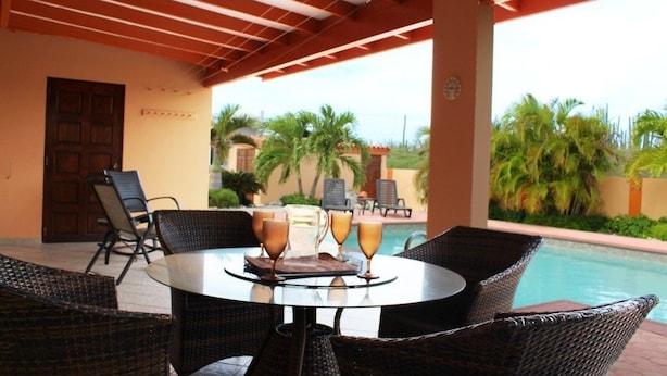 Un espacio de estar al aire libre cubierto con sillas de mimbre y una mesa redonda, con vistas a una piscina y palmeras.