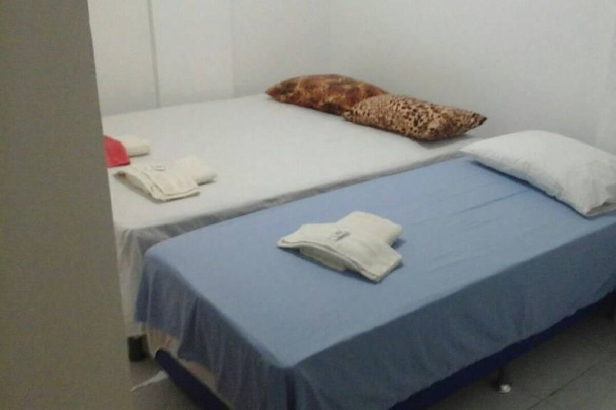 A small, simple room with two single beds, each with a pillow and a folded towel.