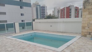 A rectangular swimming pool with a tiled deck, surrounded by a white wall and a low fence. - Pousada Beira Mar (Recife)