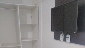 A compact room with a white wardrobe, a small white refrigerator, and a black electrical panel on the wall. - Pousada Beira Mar (Recife)