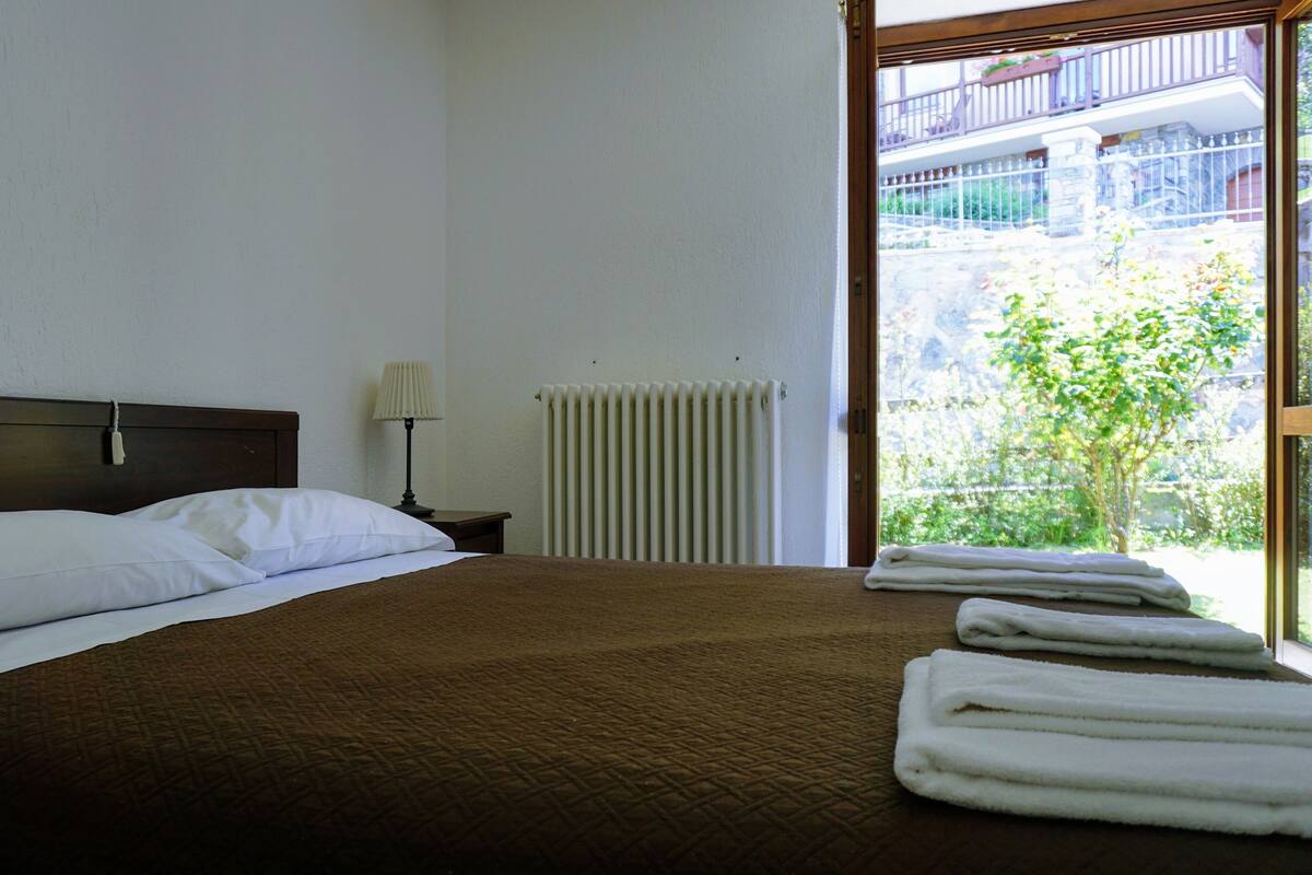 A neatly made bed with white pillows and a brown blanket, a bedside lamp, and a radiator.