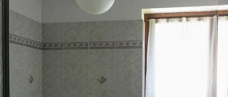 Un baño con inodoro, bidé y lavamanos, paredes con azulejos y una ventana con cortinas.