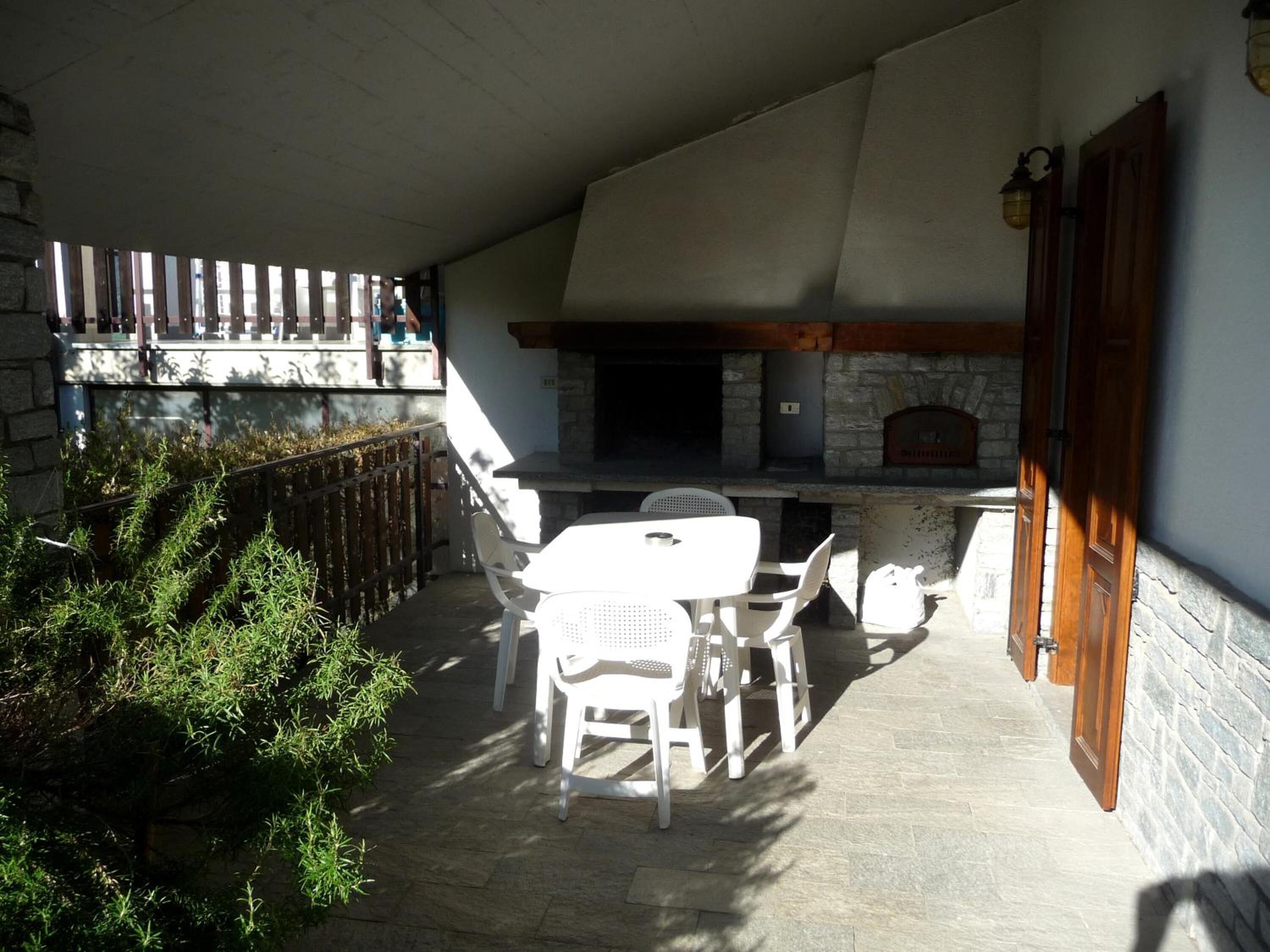 An outdoor patio with a stone fireplace, white plastic chairs, and a table.