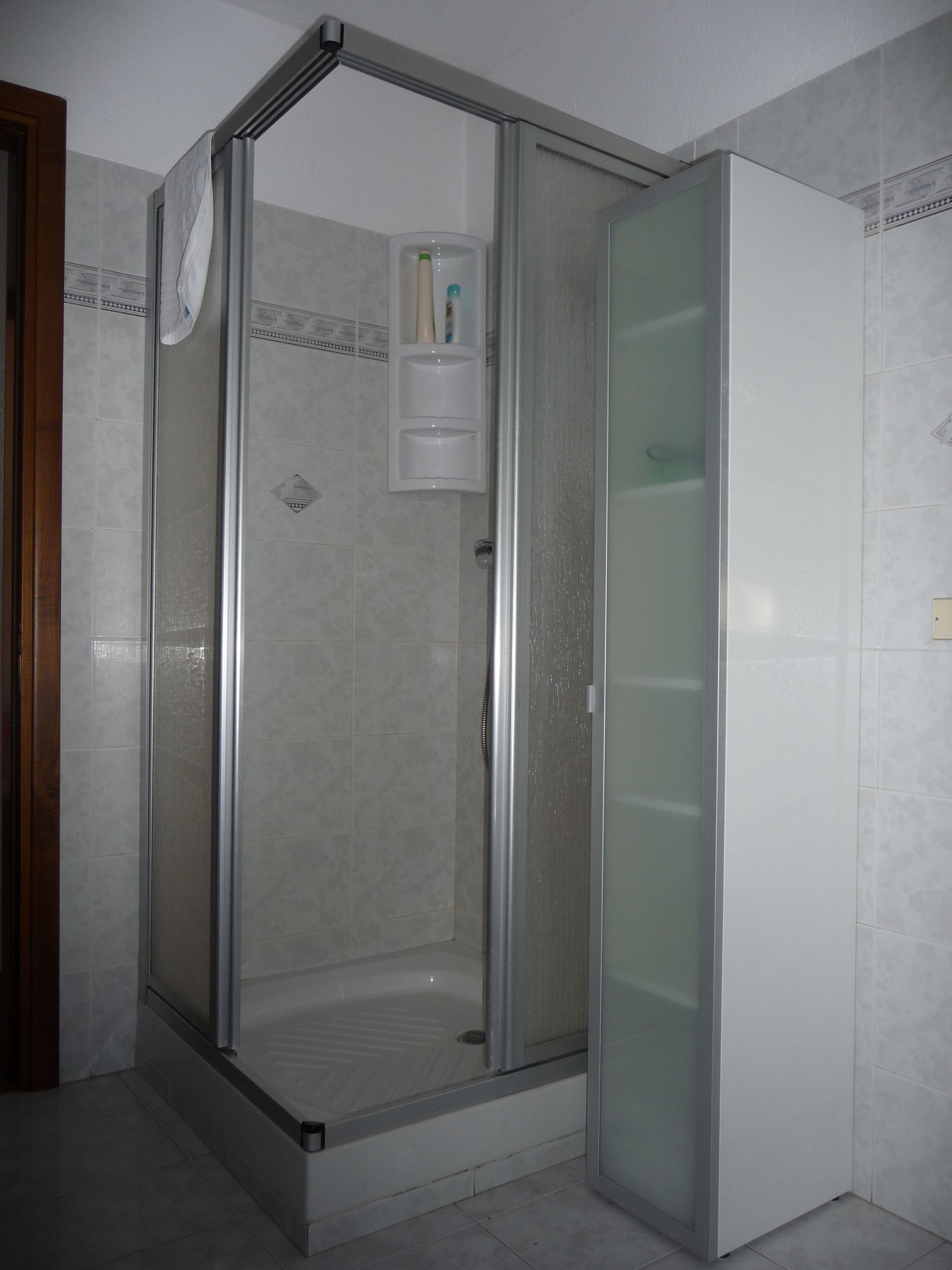 Un box de ducha con paredes de vidrio, piso de baldosas y un estante pequeño con artículos de tocador.
