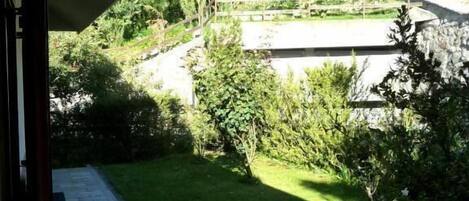 A patio area with a stone floor, surrounded by greenery and a view of a landscaped garden.