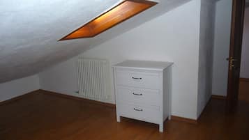 A room with a sloped ceiling, a radiator, a white dresser with drawers, and a door.