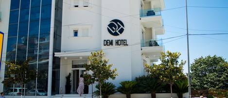 Hotel modern amb un logotip destacat, una escala que condueix a l'entrada i una façana ben cuidada amb plantes en testos.