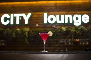 A martini glass with a garnish on a bar counter, with a 'CITY lounge' sign in the background. - Demi Hotel (Sarandë)