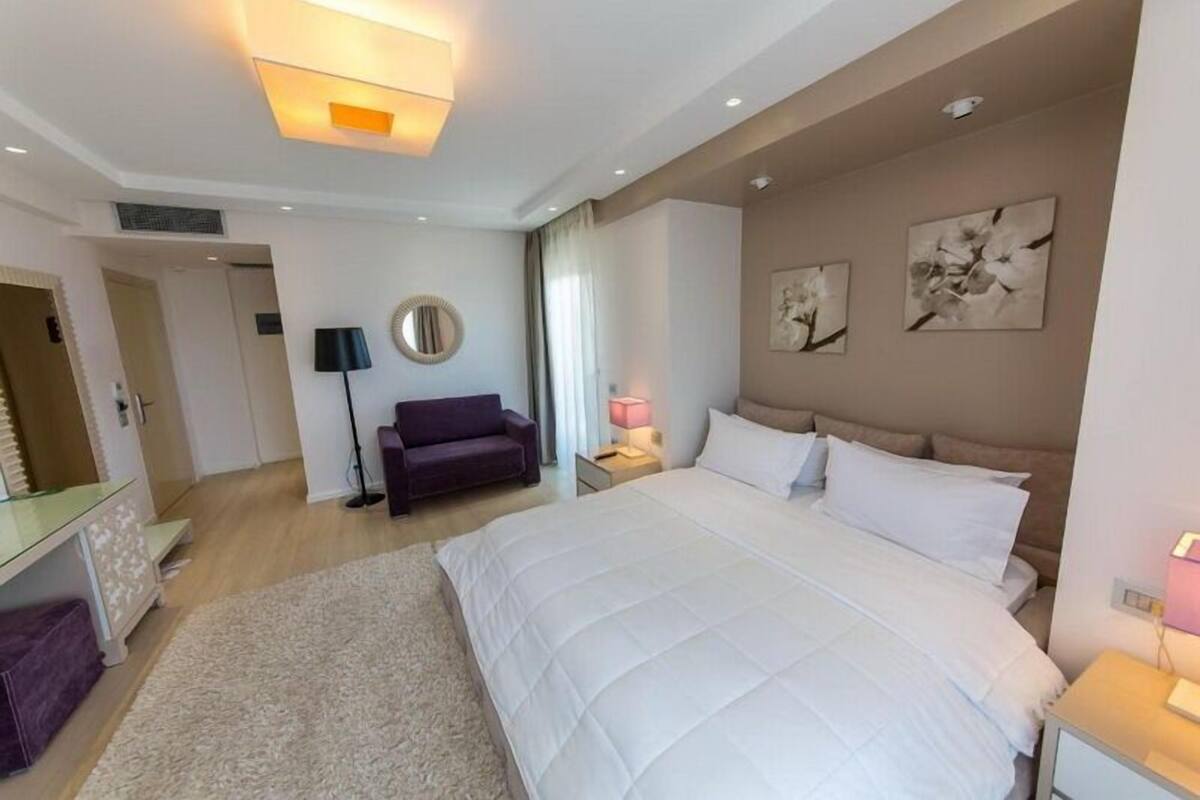 A modern hotel room with a large bed, a sofa, a desk, and a mirror.