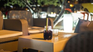 Un coin repas avec des meubles en osier et une table sur laquelle se trouvent une boisson et un verre.