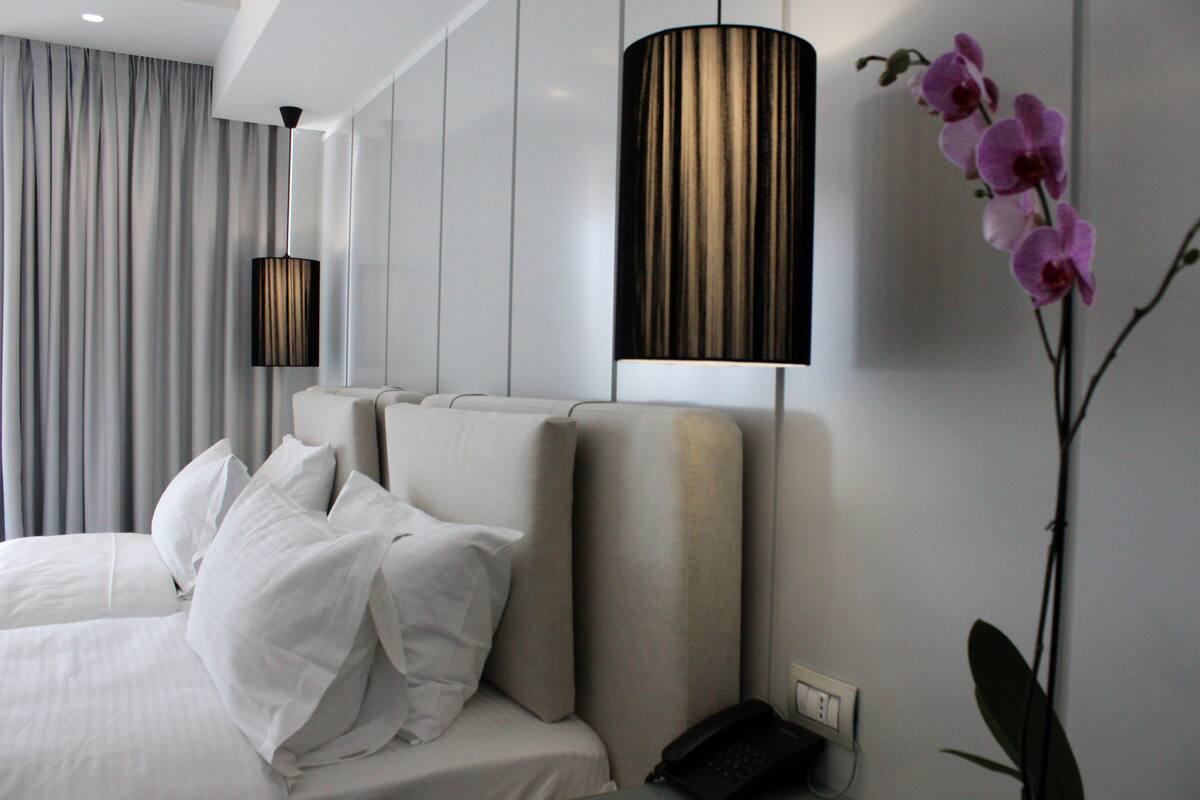 A modern hotel room with a large bed, a bedside lamp, and a potted orchid.