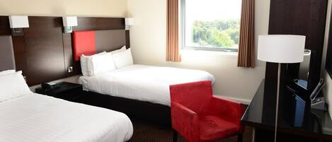 A hotel room with two beds, a red chair, a desk with a lamp, and a window with curtains.