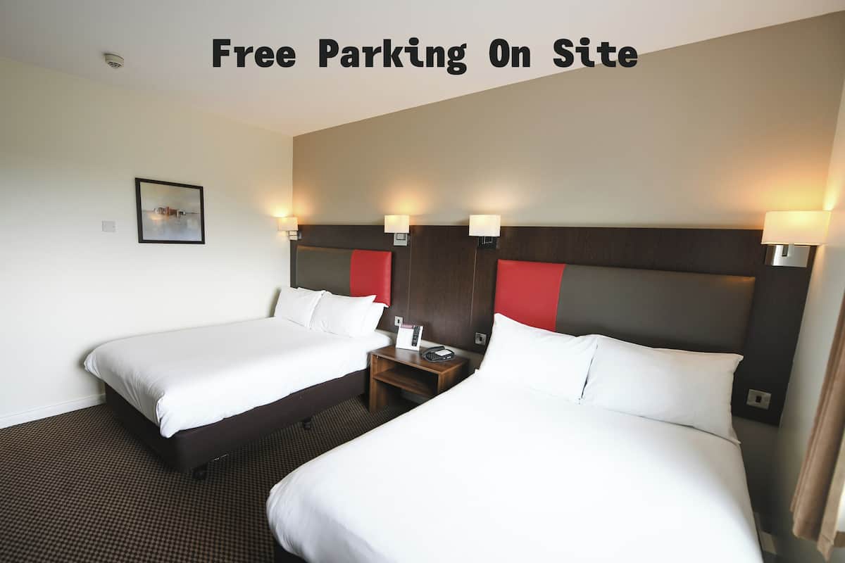 A hotel room with two beds, a nightstand, and a wall-mounted lamp.
