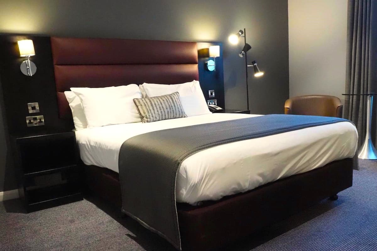 A hotel room with a large bed, dark headboard, bedside lamps, and a nightstand.