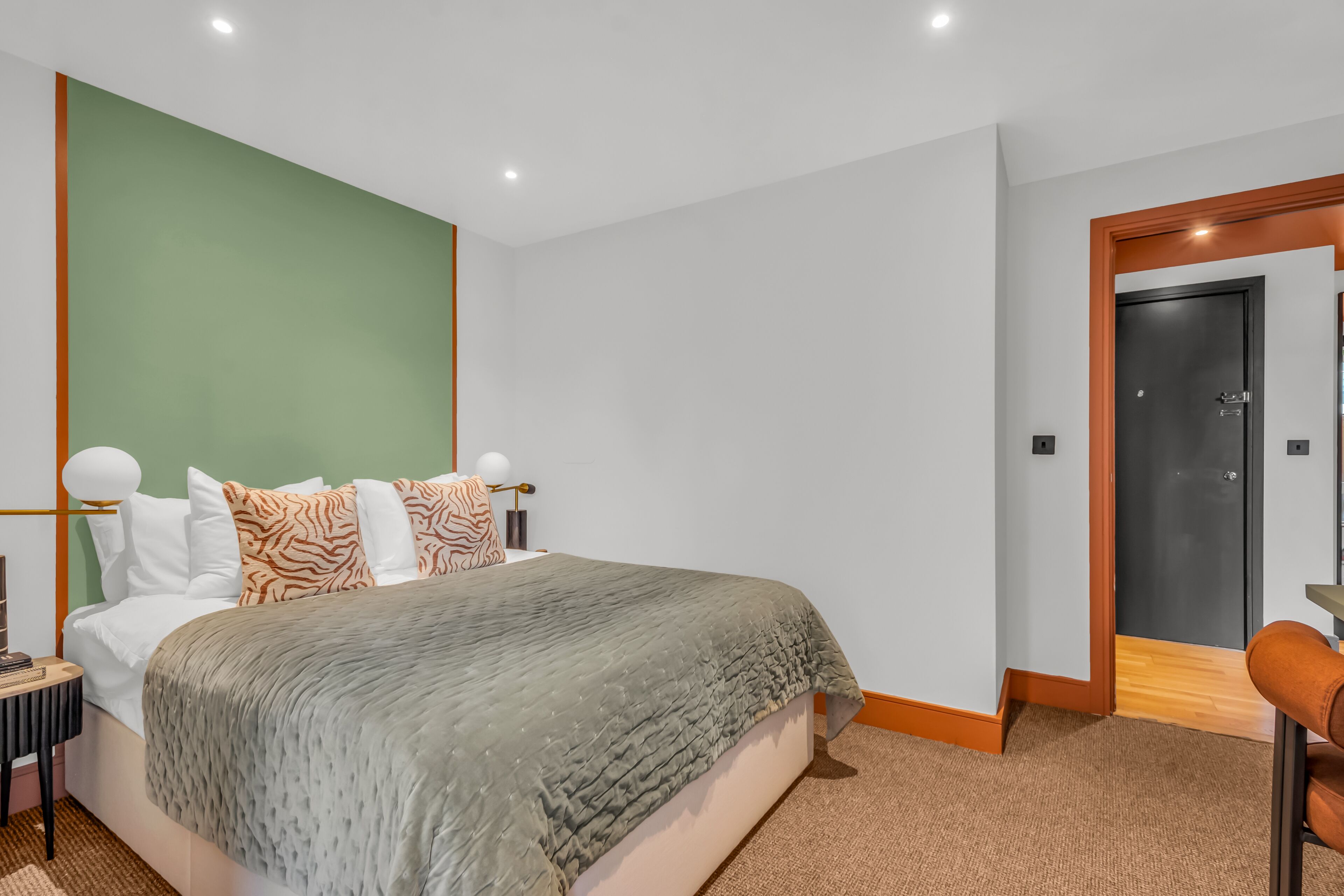 A modern bedroom with a bed, green accent wall, and a door to another room.