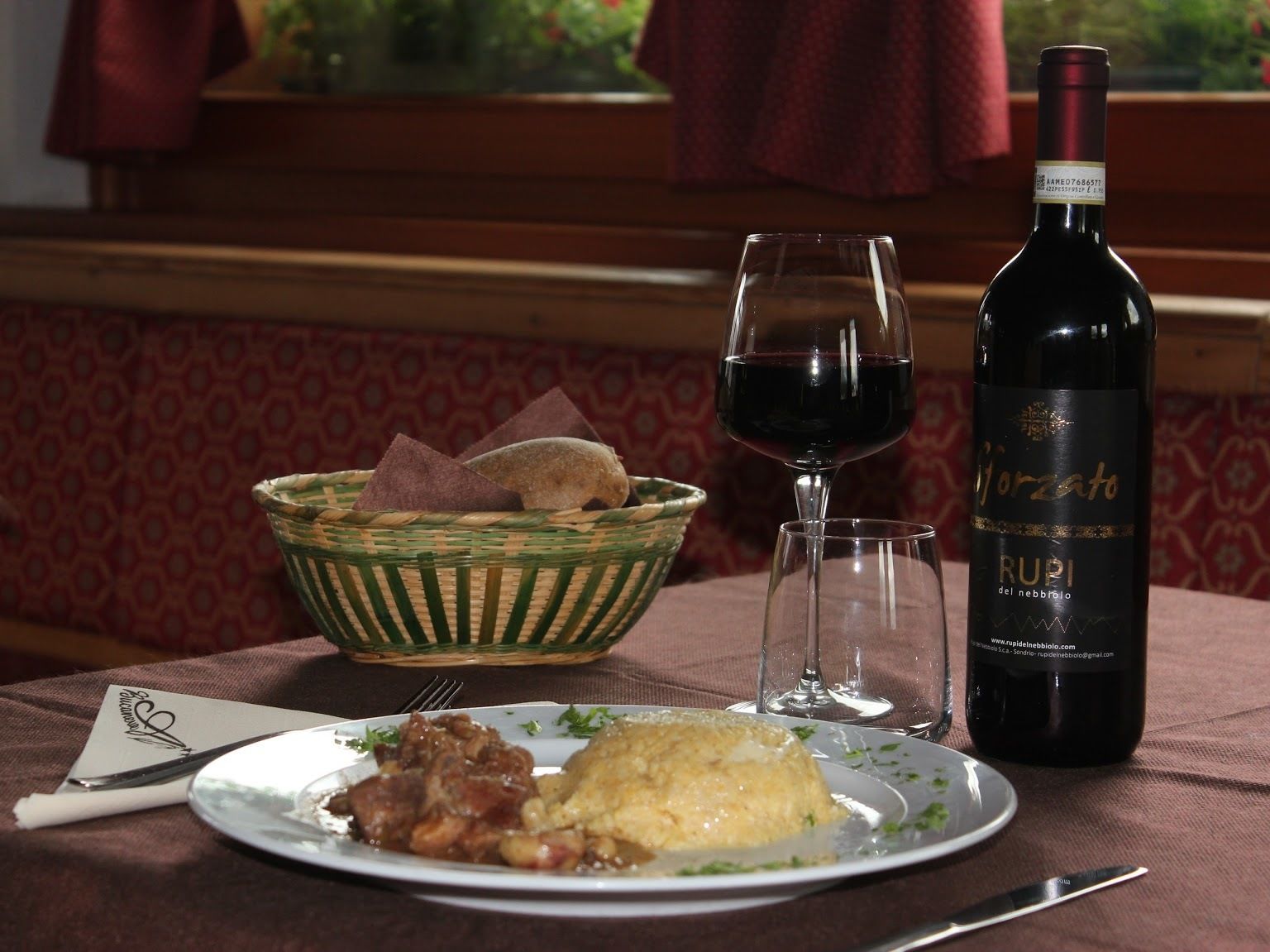 A dining table with a plate of food, a bottle of wine, and a glass of red wine.