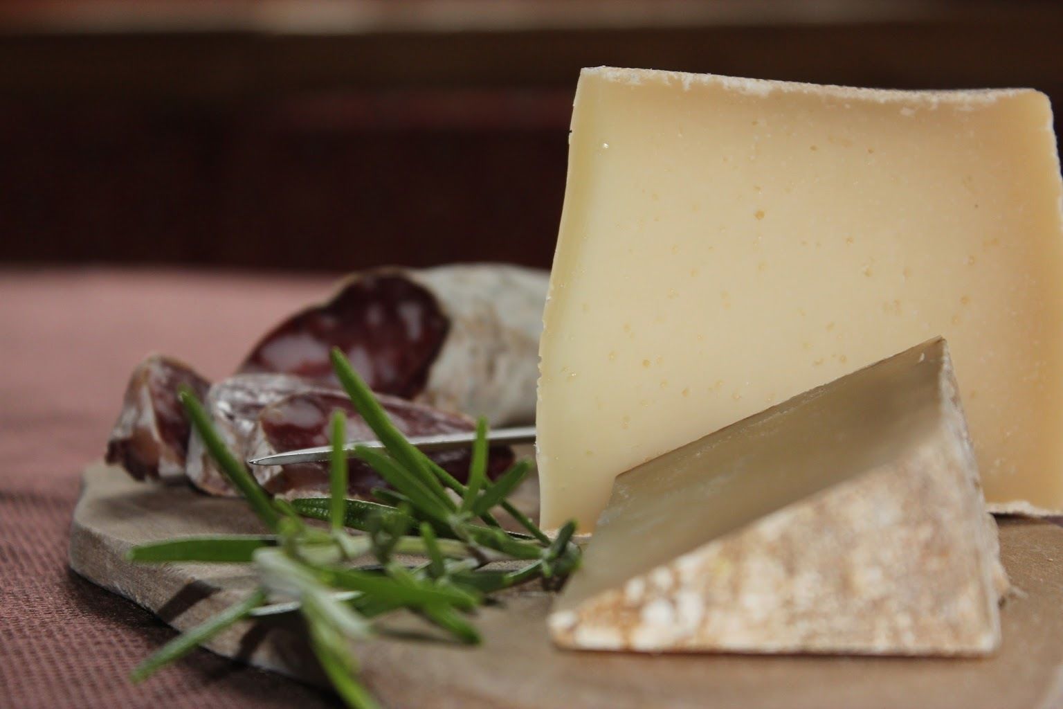 Un assortiment de fromages et de charcuteries, présentés sur une planche en bois et décorés de brins de romarin.