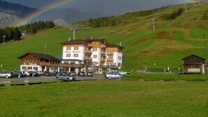 A building with a sign reading "Allergo Bueche," a bar, and restaurant. There are cars parked in front. - Bucaneve (Campodolcino)