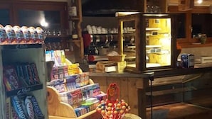 A rustic interior with wooden beams, a counter displaying snacks and beverages, and shelves stocked with various items. - Bucaneve (Campodolcino)