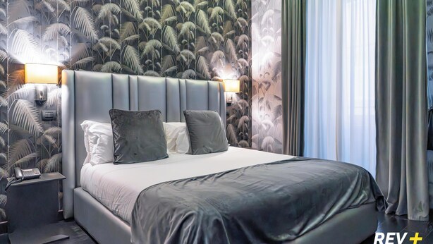 A modern hotel room with a large bed, two bedside lamps, and a patterned wallpaper. - Via Veneto Suites (Rome)