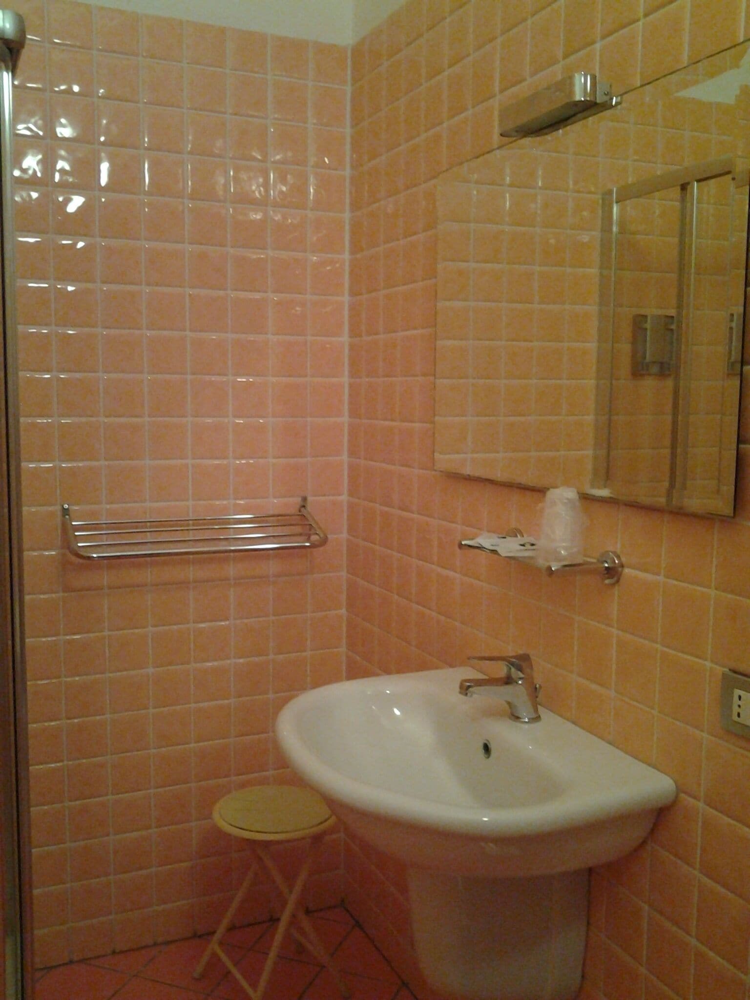 Un bagno con lavandino, specchio e uno sgabello.