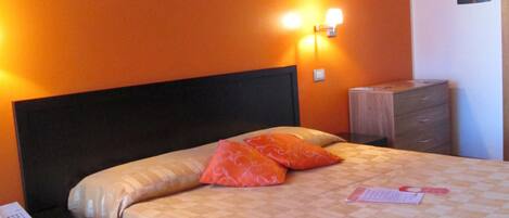 Habitación de hotel con cama, mesita de noche, cómoda y unidad de aire acondicionado en la pared.