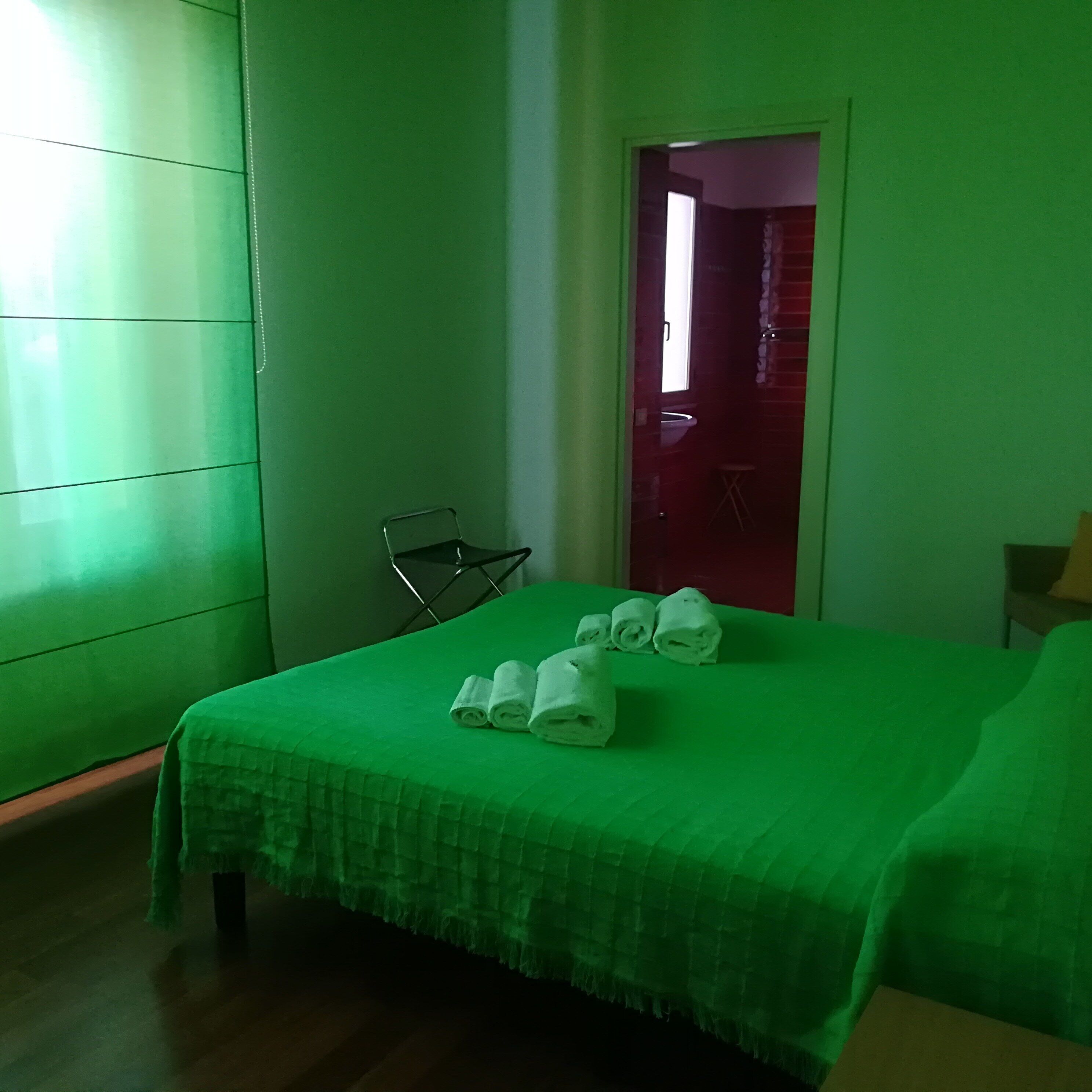 A room with a green bedspread, a chair, and a door leading to another room.