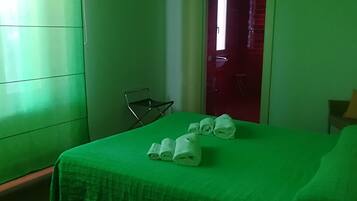 A room with a green bedspread, a chair, and a door leading to another room.
