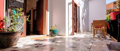 A narrow corridor with a tiled floor, wooden doors, and potted plants.