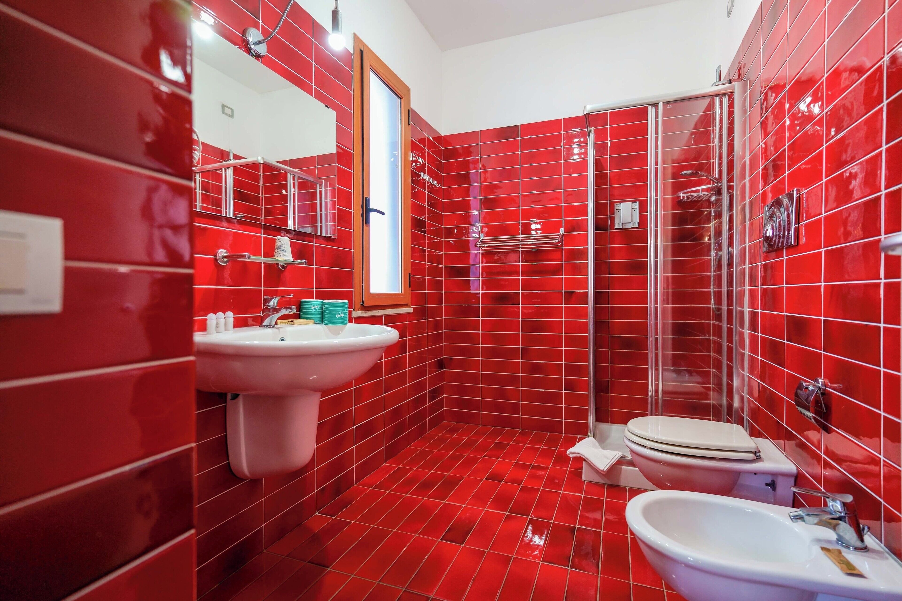 A bathroom with red tiles, a sink, a toilet, and a shower.