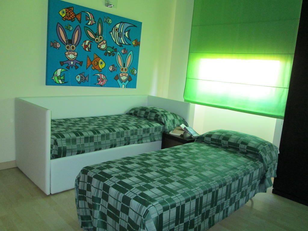 A room with two single beds, a wall-mounted artwork, and a window with a green blind.