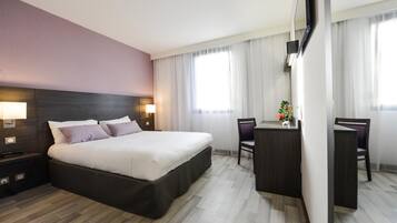A hotel room with a large bed, bedside tables, a desk, and chairs.