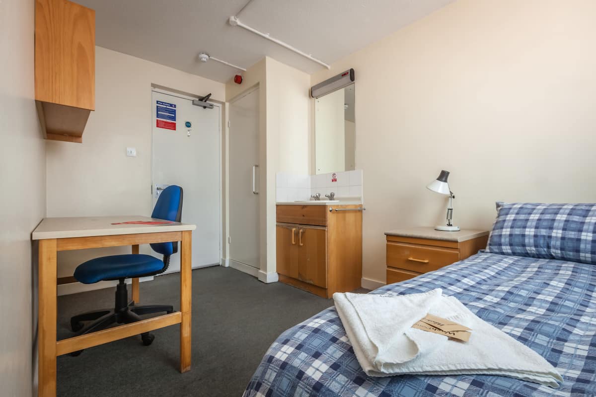Une chambre d’hôtel comprenant un lit, un bureau avec une chaise, une petite table de chevet avec une lampe et une armoire.