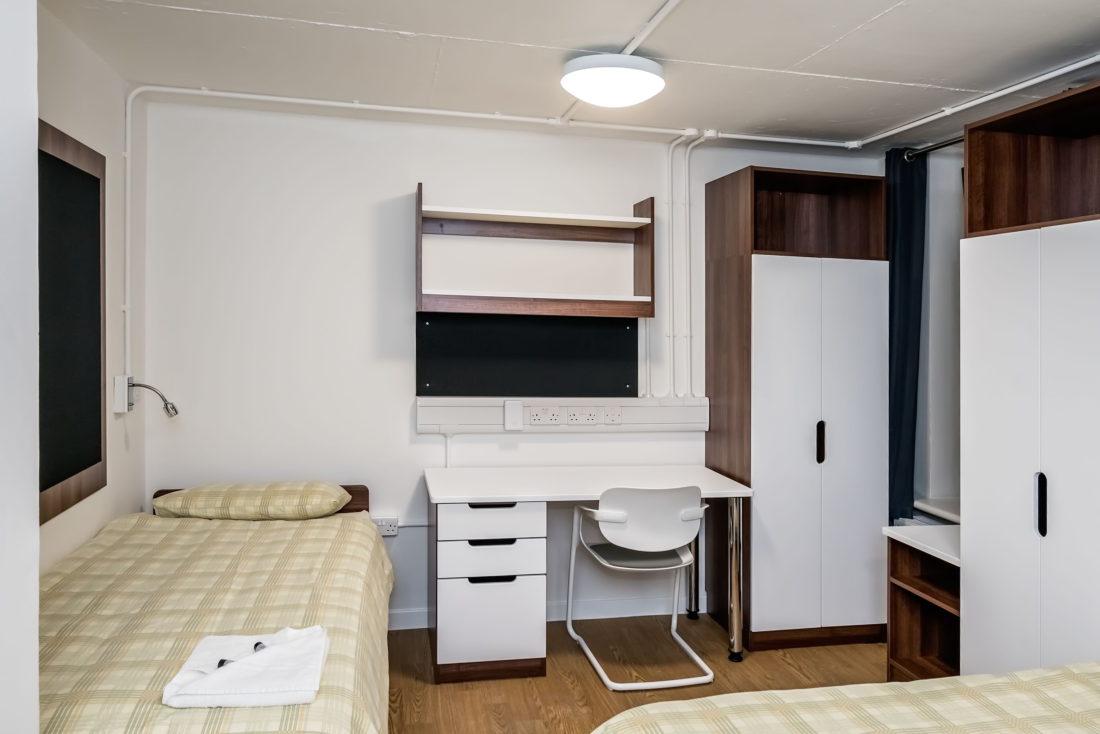 A bedroom with a bed, a desk, and a wardrobe.