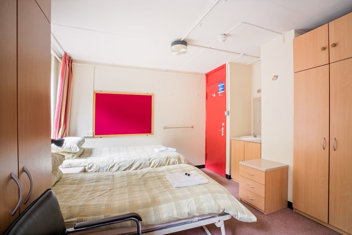 Une chambre d’hôtel avec deux lits, un mur rouge, une armoire en bois et une petite salle de bain.